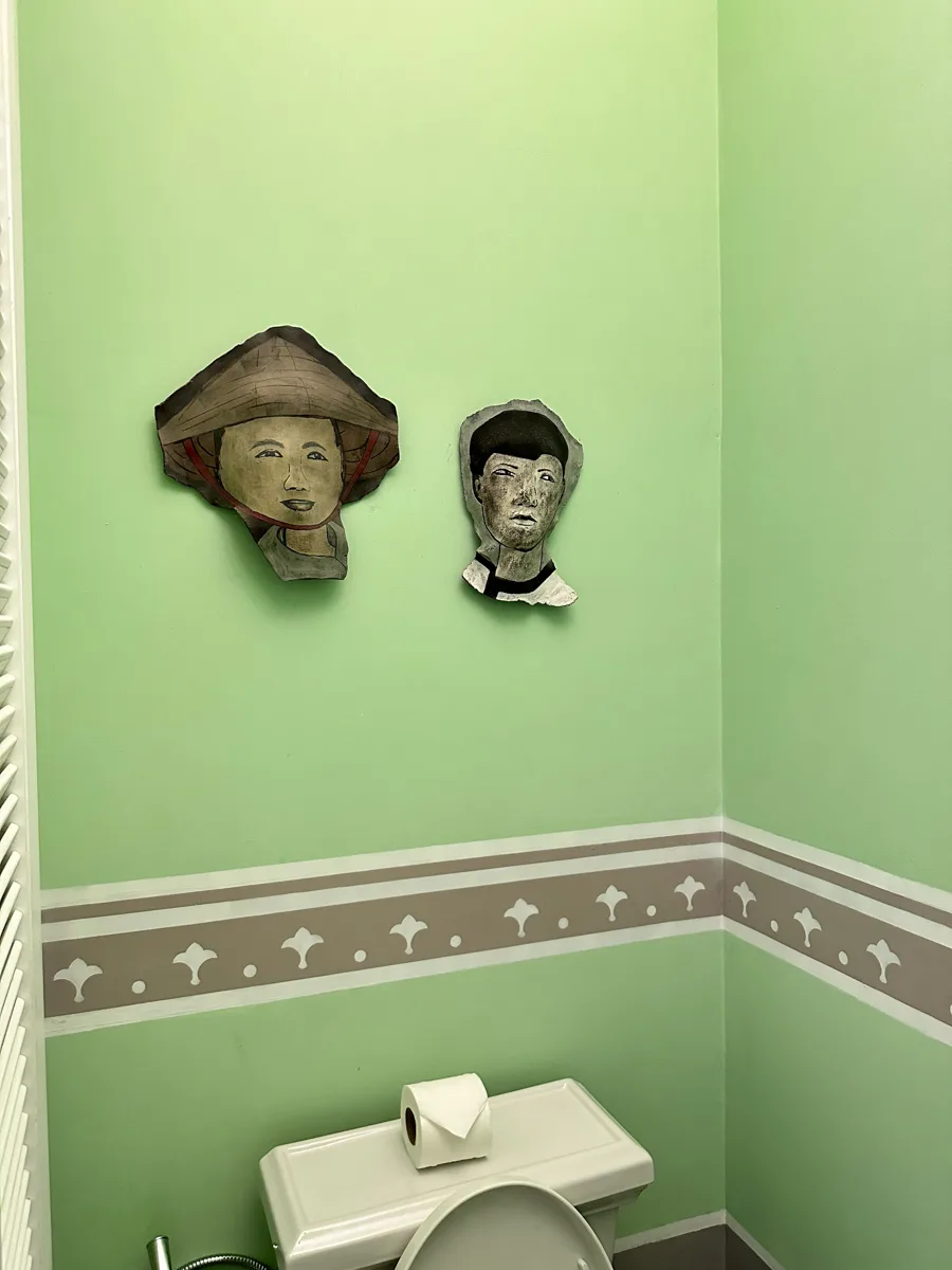 Two carved 3D face masks — a woman in a conical Vietnamese hat and a man — mounted in the bathroom of a JW Marriott Phu Quoc double room