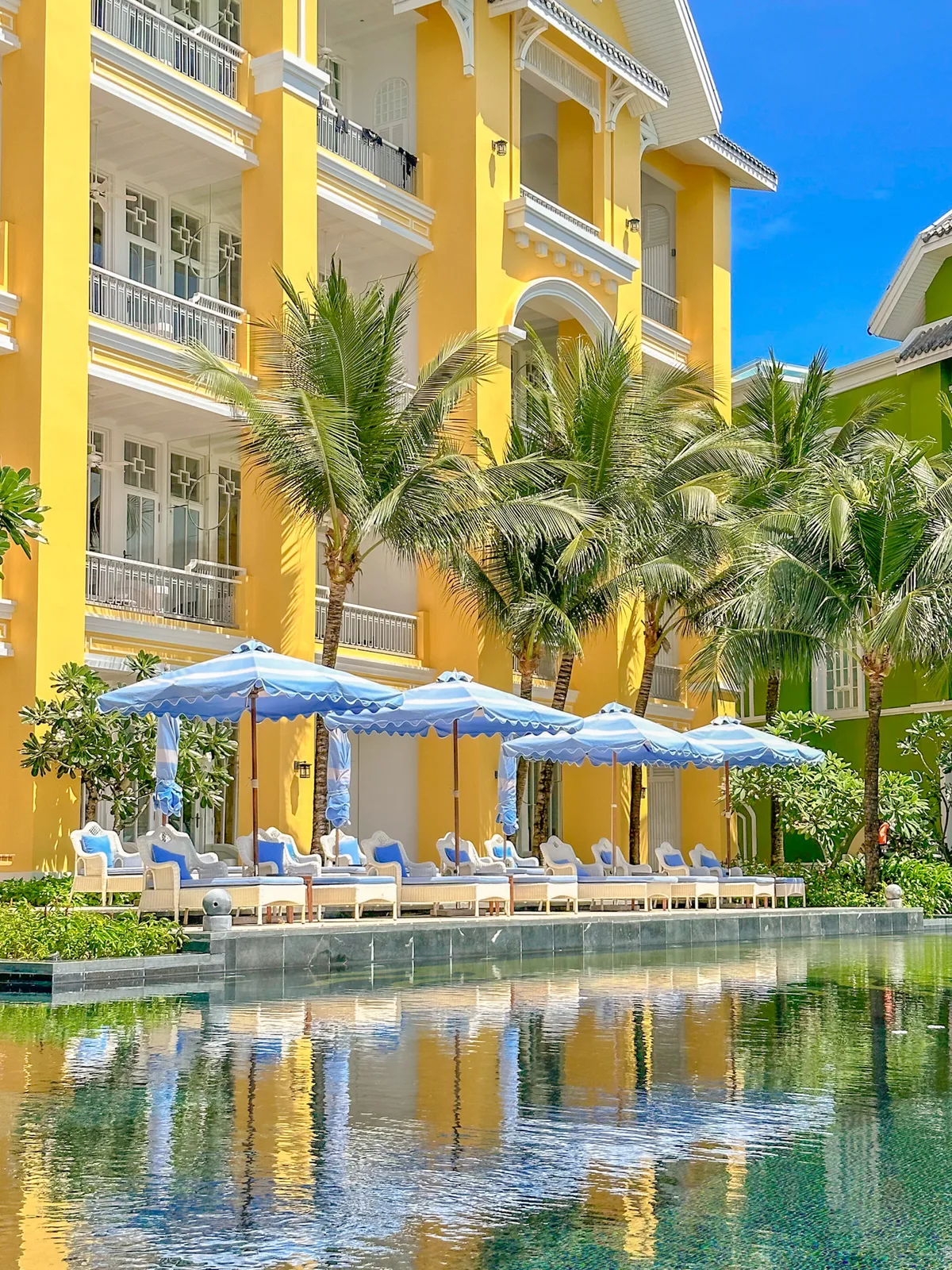 Colorful campus buildings reflected in the pool at JW Marriott Phu Quoc, with striped loungers along the edge