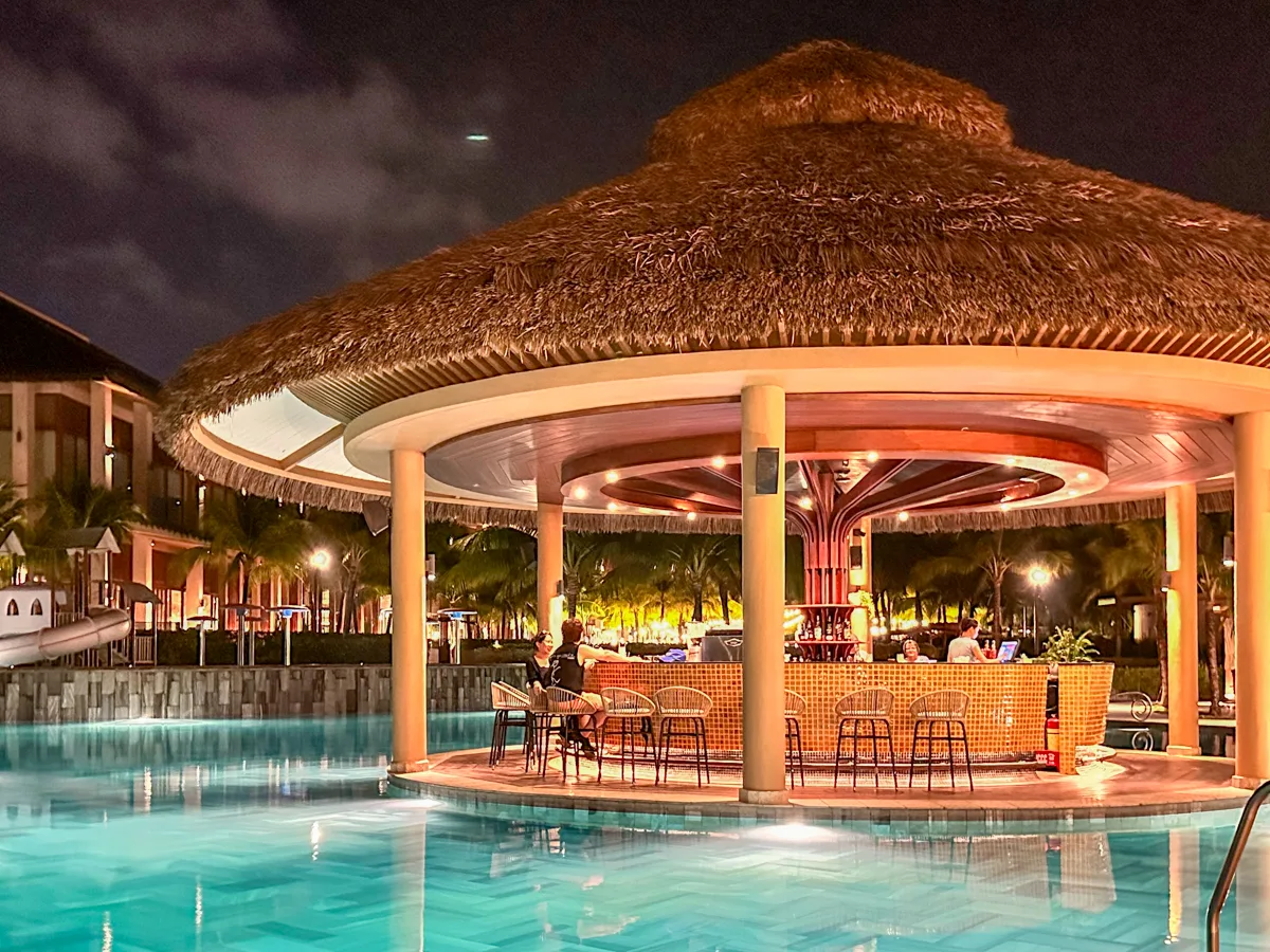 Thatched-roof pool bar lit up at night at New World Phu Quoc Resort