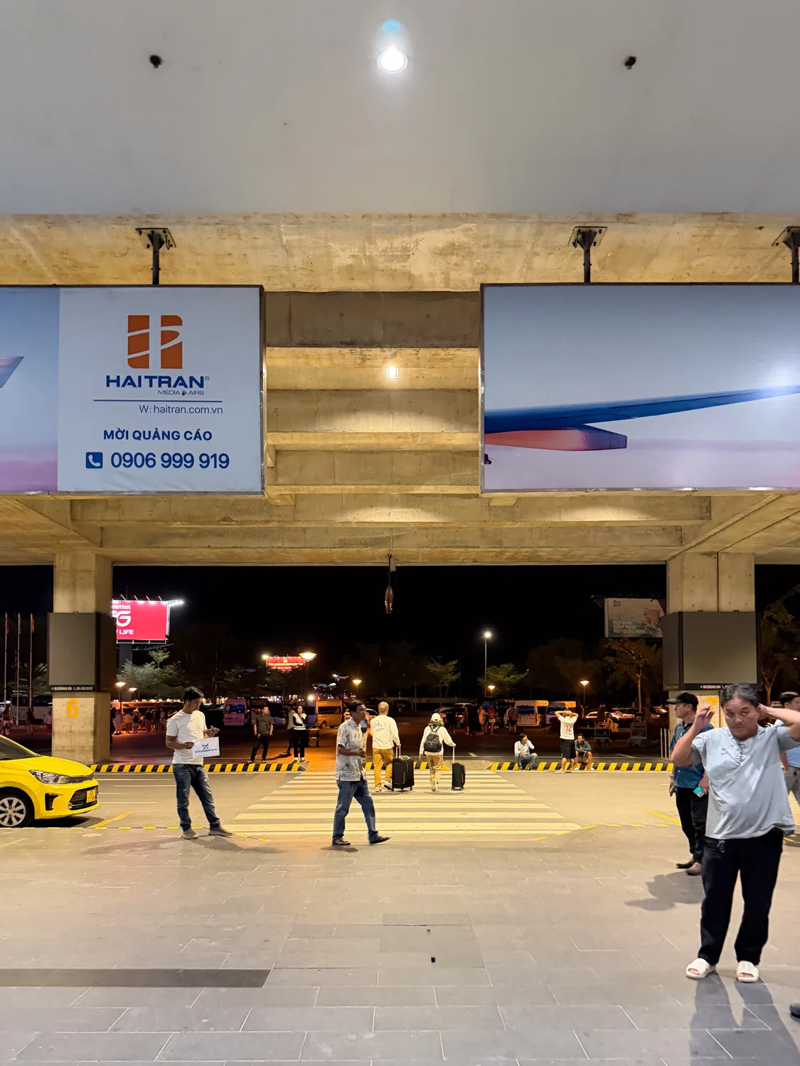 Grab pickup zone with a taxi and travelers crossing at night outside Phu Quoc International Airport