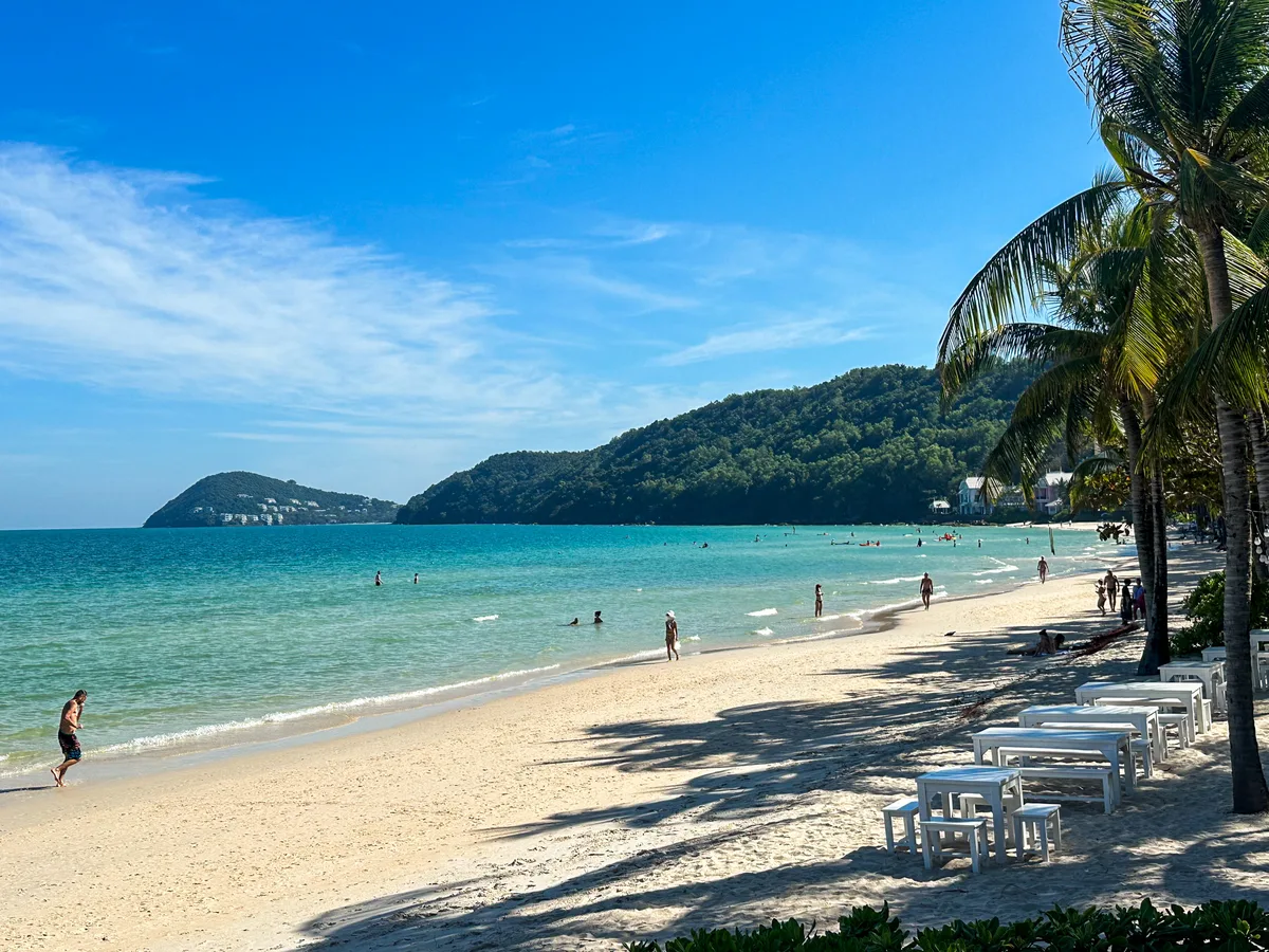 Sunlit, busy Phu Quoc beach with hills and a bay in the background