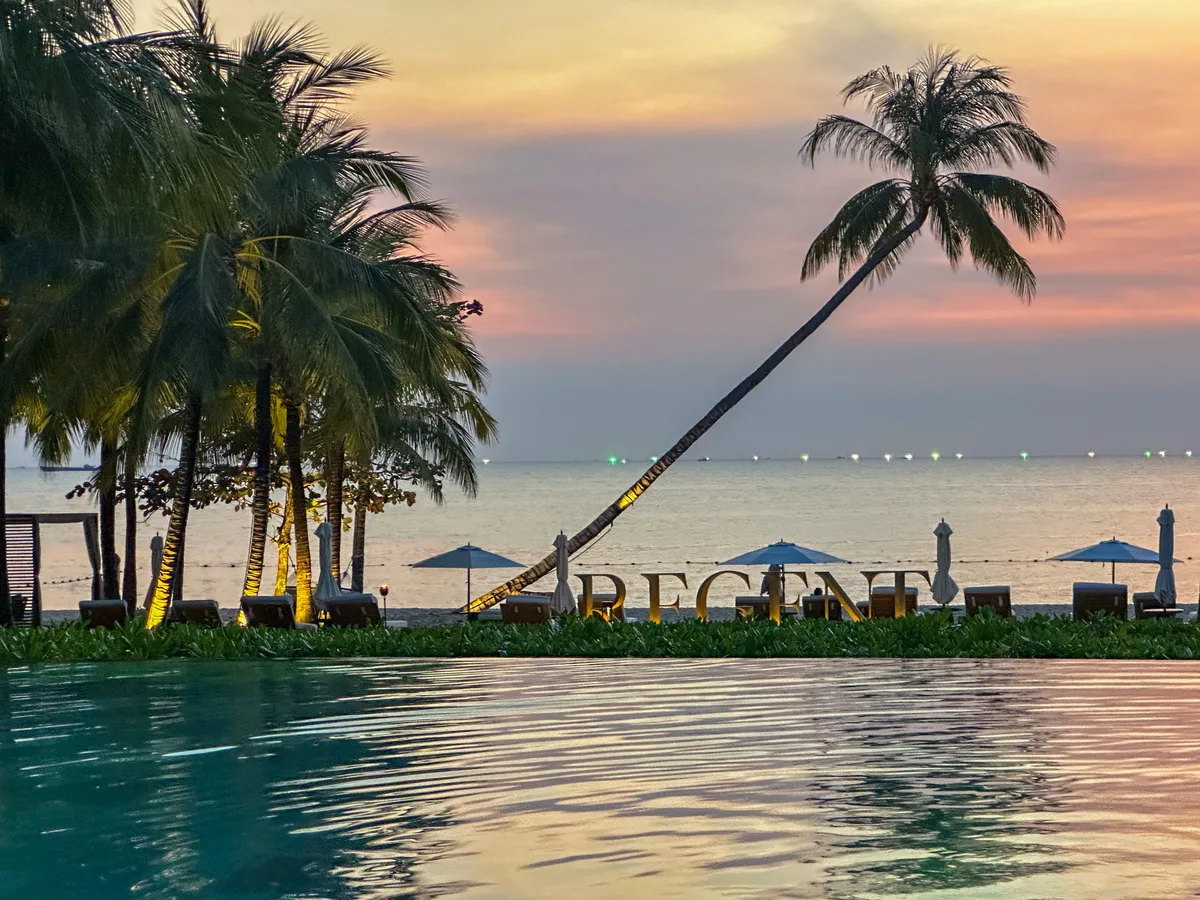 Sunset over a Phu Quoc beach with palm silhouettes and a still infinity pool