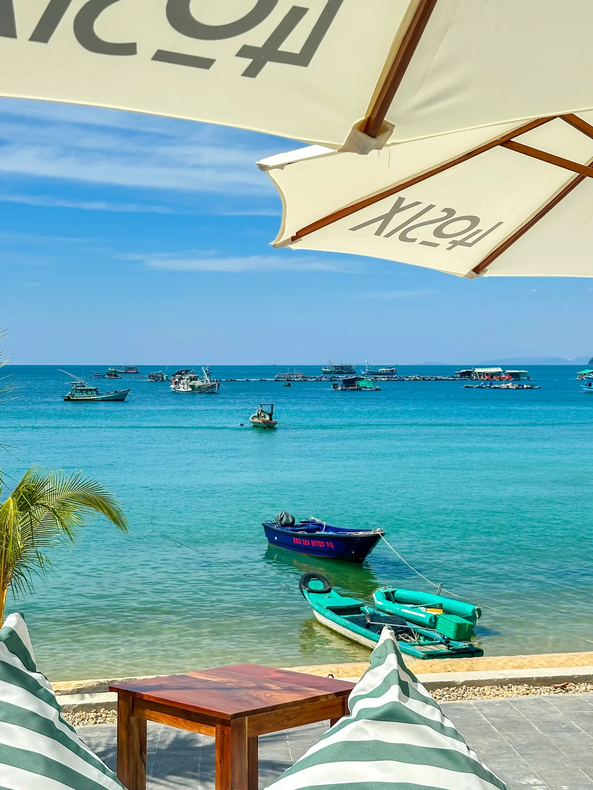 Fishing-village view from under a beach umbrella with boats anchored on calm water